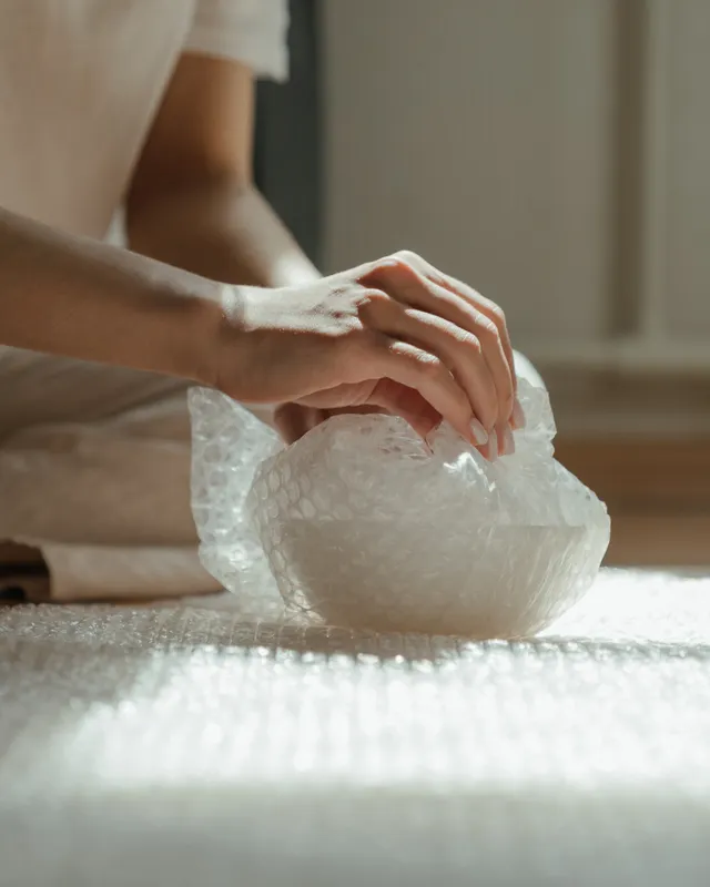 Hender som pakker en skål forsiktig inn i bobleplast